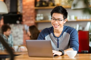 Happy cheerful young asian male in glasses smiling and using laptop in cafe.jpeg