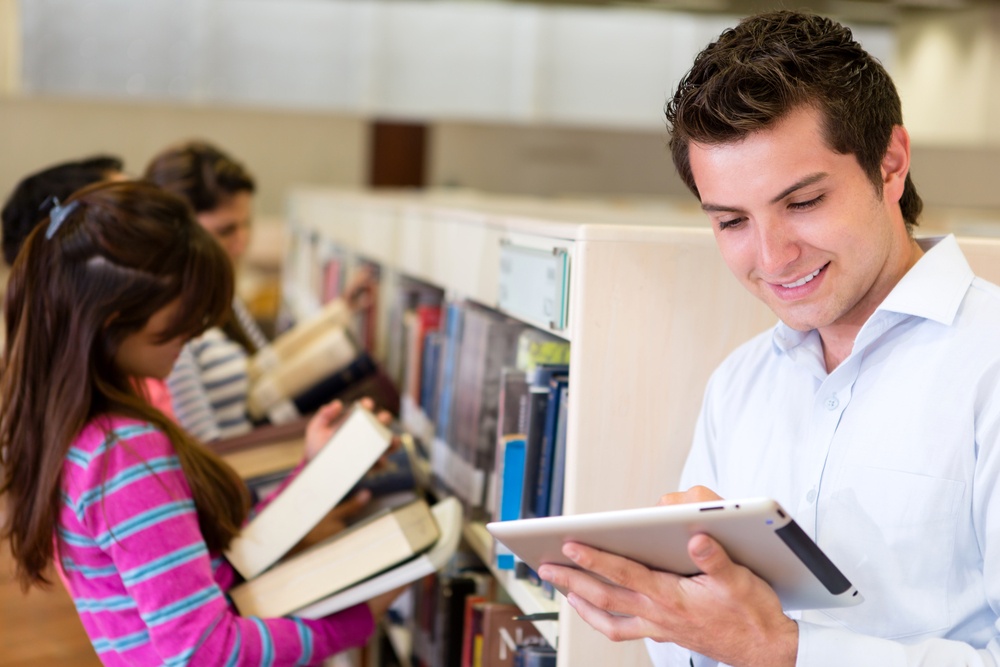 Man with an e-book reader while his friends look for books at the library.jpeg